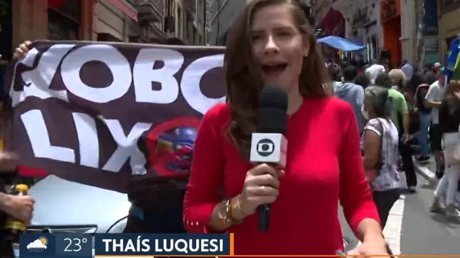 Repórter tenta driblar cartaz de “Globo Lixo”, ao vivo, durante telejornal