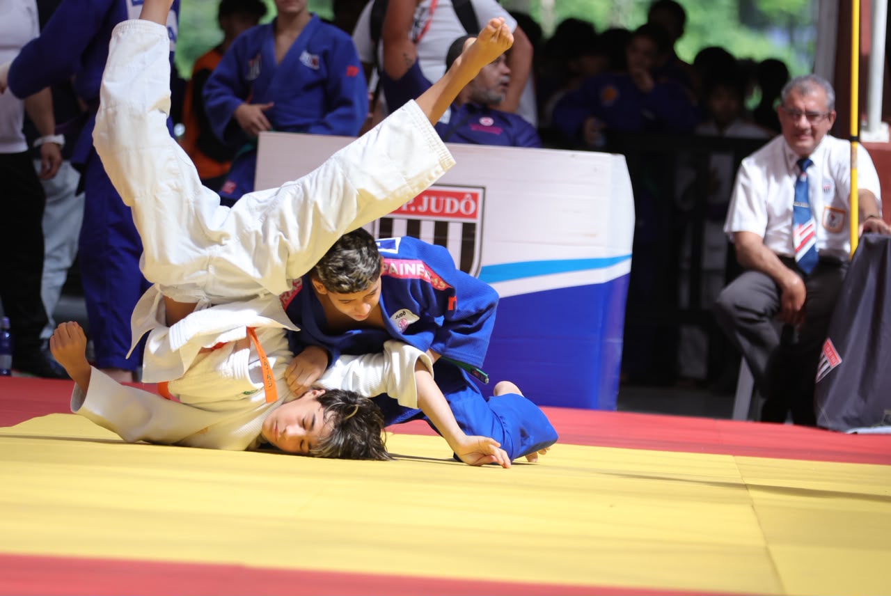 Texto alternativo: Lorenzo Floriano, de judo azul, disputa uma luta de judô contra um atleta de judo branco sobre o tatame.