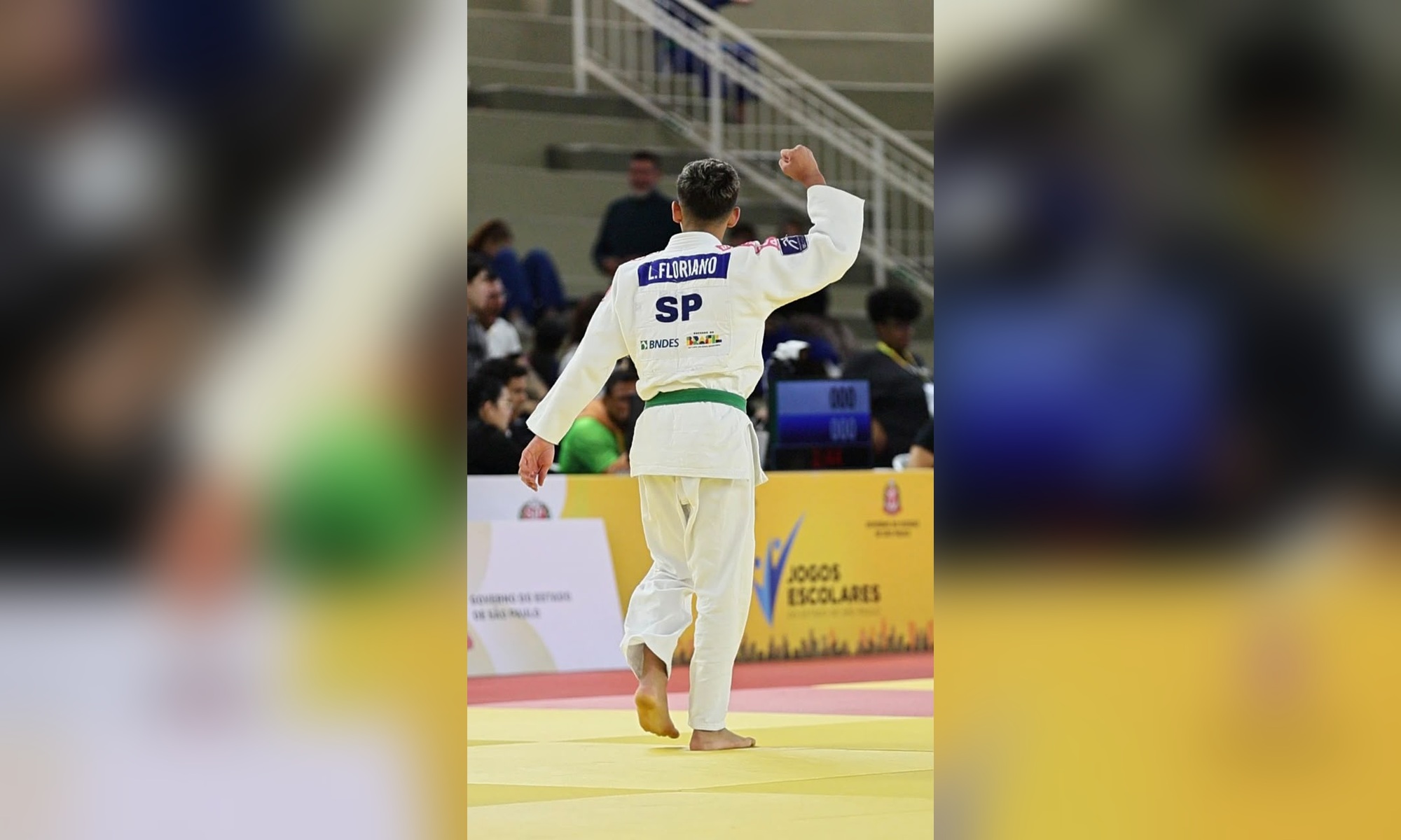 Lorenzo Floriano, de judogi branco e faixa verde, ergue o braço durante competição de judô.
